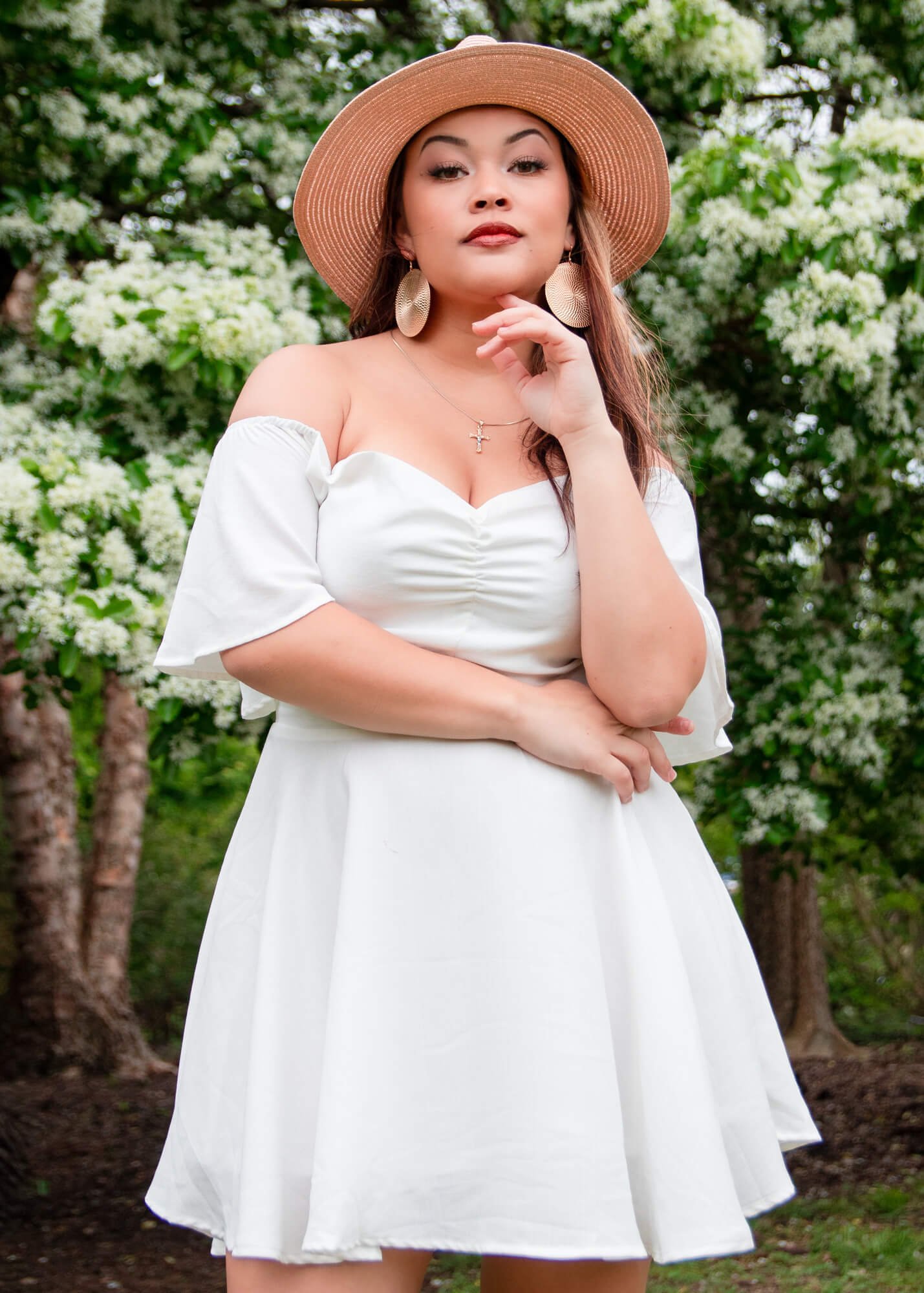 A model poses in a white drive and straw hat during a portrait session at JC Raulston Arboretum in Raleigh, NC