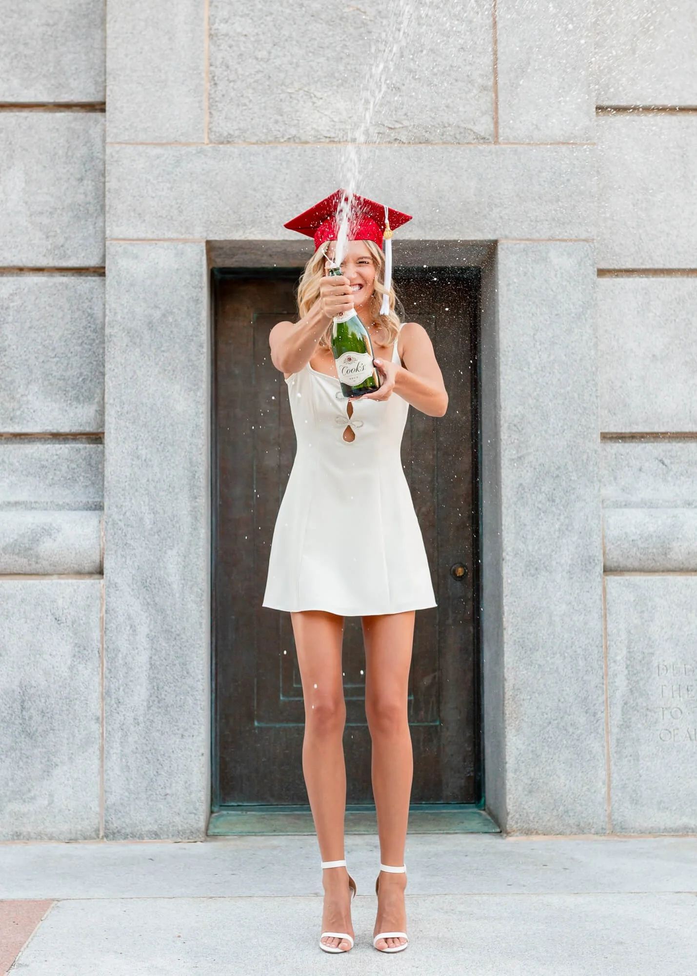An NC State University student pops a bottle of champagne during her graduation portrait session in Raleigh, NC.  The session was photographed by PixByDez Photography.