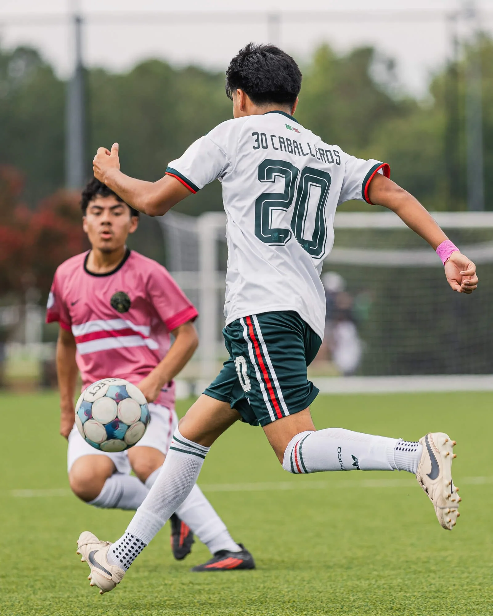 A soccer player prepares to kick the ball over an opposing player during a soccer game in Raleigh, NC. The photograph was taken by PixByDez Photography, a sports photographer based in Raleigh, NC