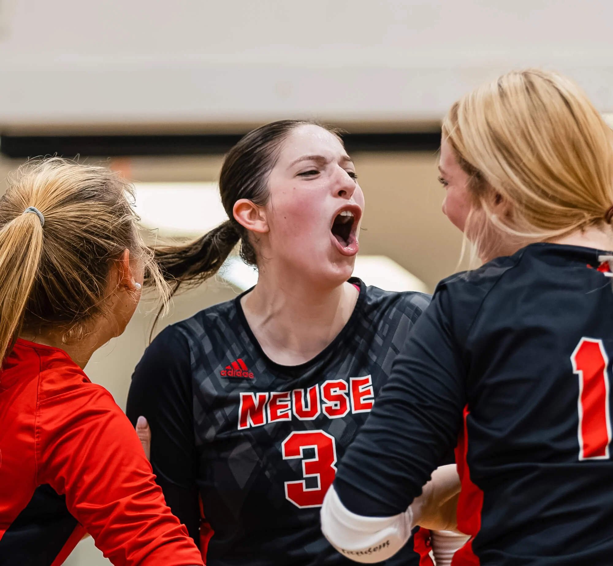 A female volleyball player celebrates with her team after a point during a high school volleyball game in Raleigh, NC.  The photo was photographed by PixByDez Photography