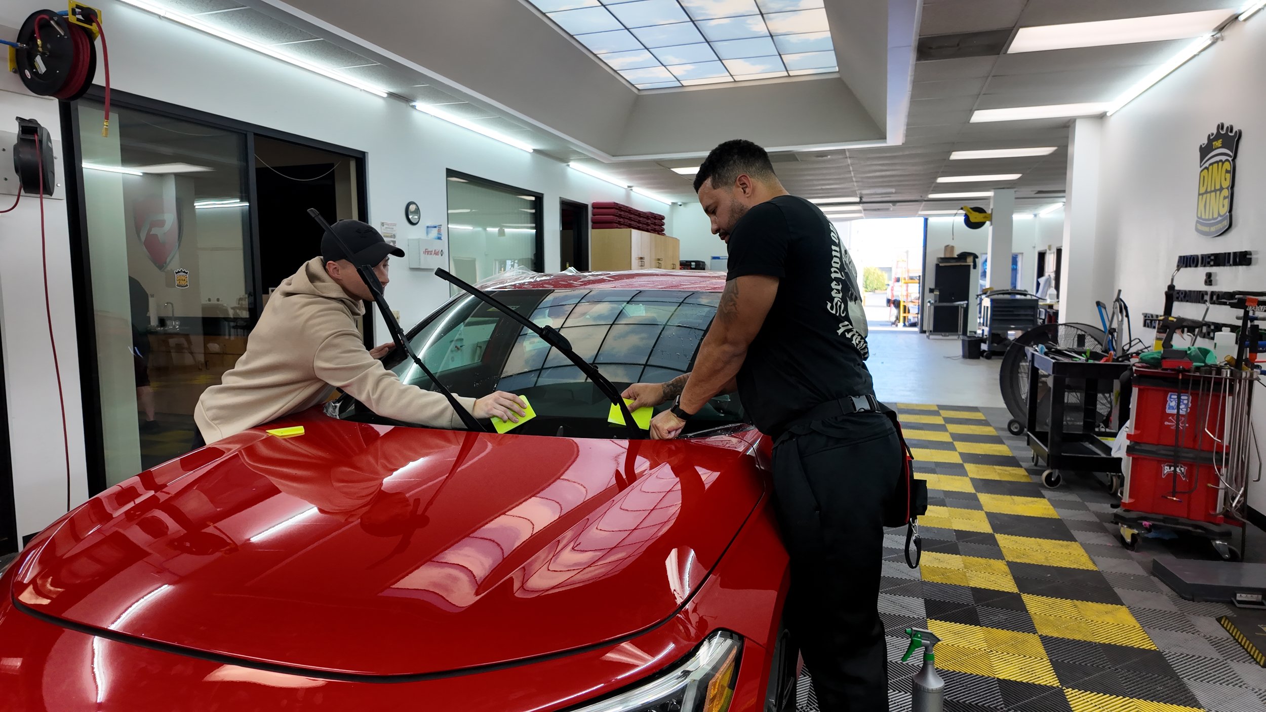 echnician using a squeegee to smooth paint protection film on a vehicle fender during a precision PPF installation.