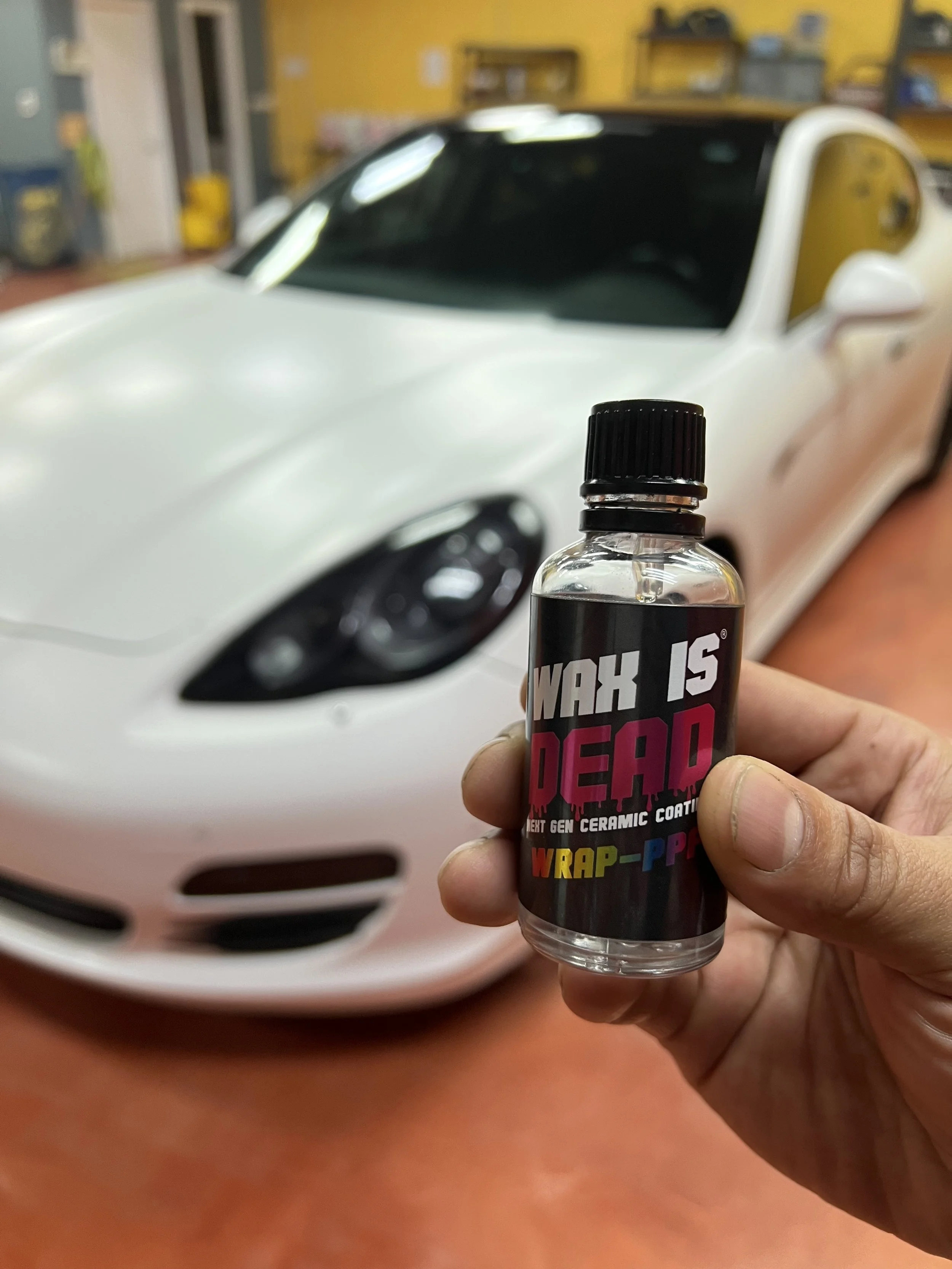 Technician finishing a ceramic coating treatment on a black car to enhance shine and provide long term durability.