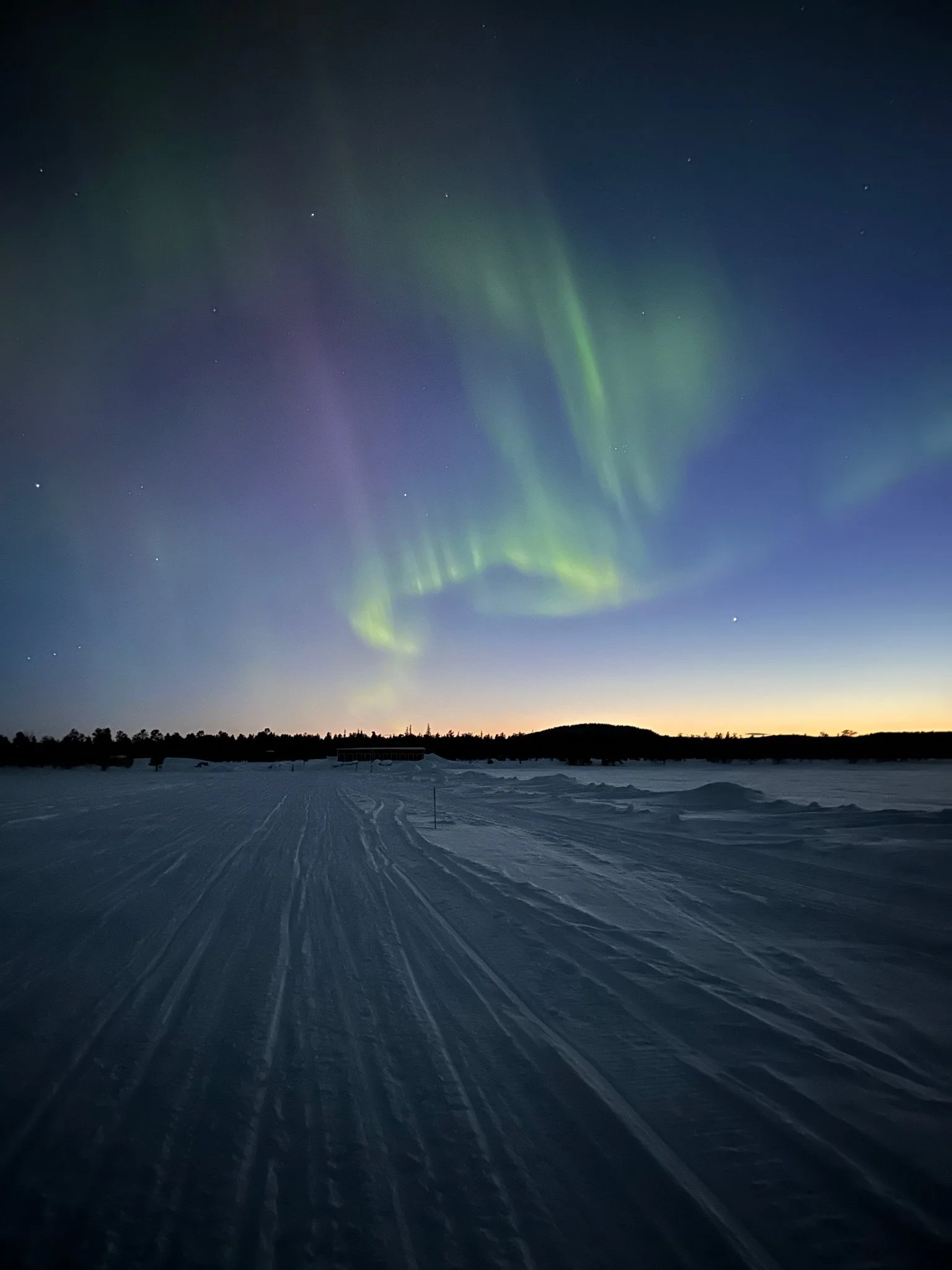 Northern lights over snow-covered landscape at dusk with a clear sky.