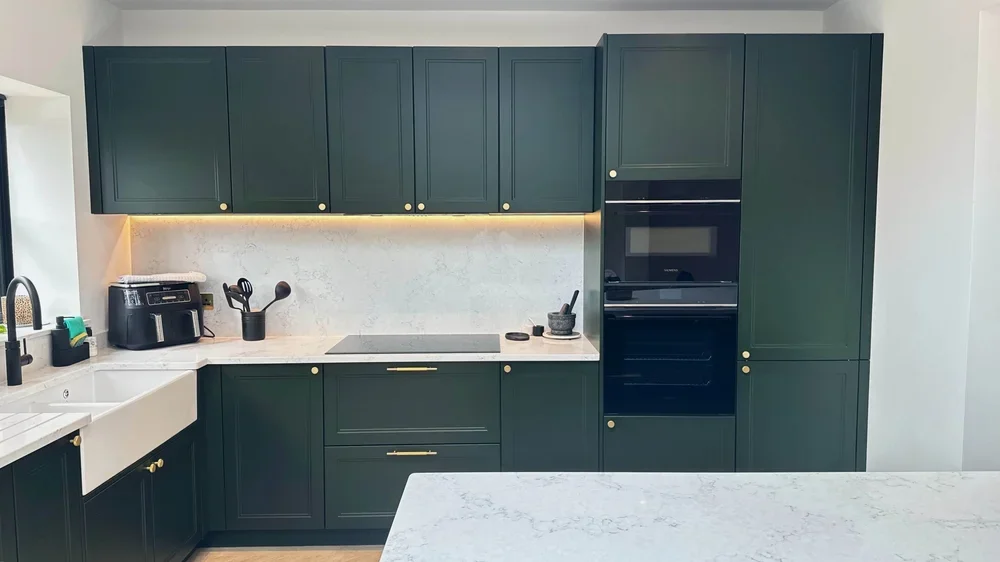 Modern kitchen with green cabinets, white countertop, induction cooktop, black oven, and air fryer on counter.