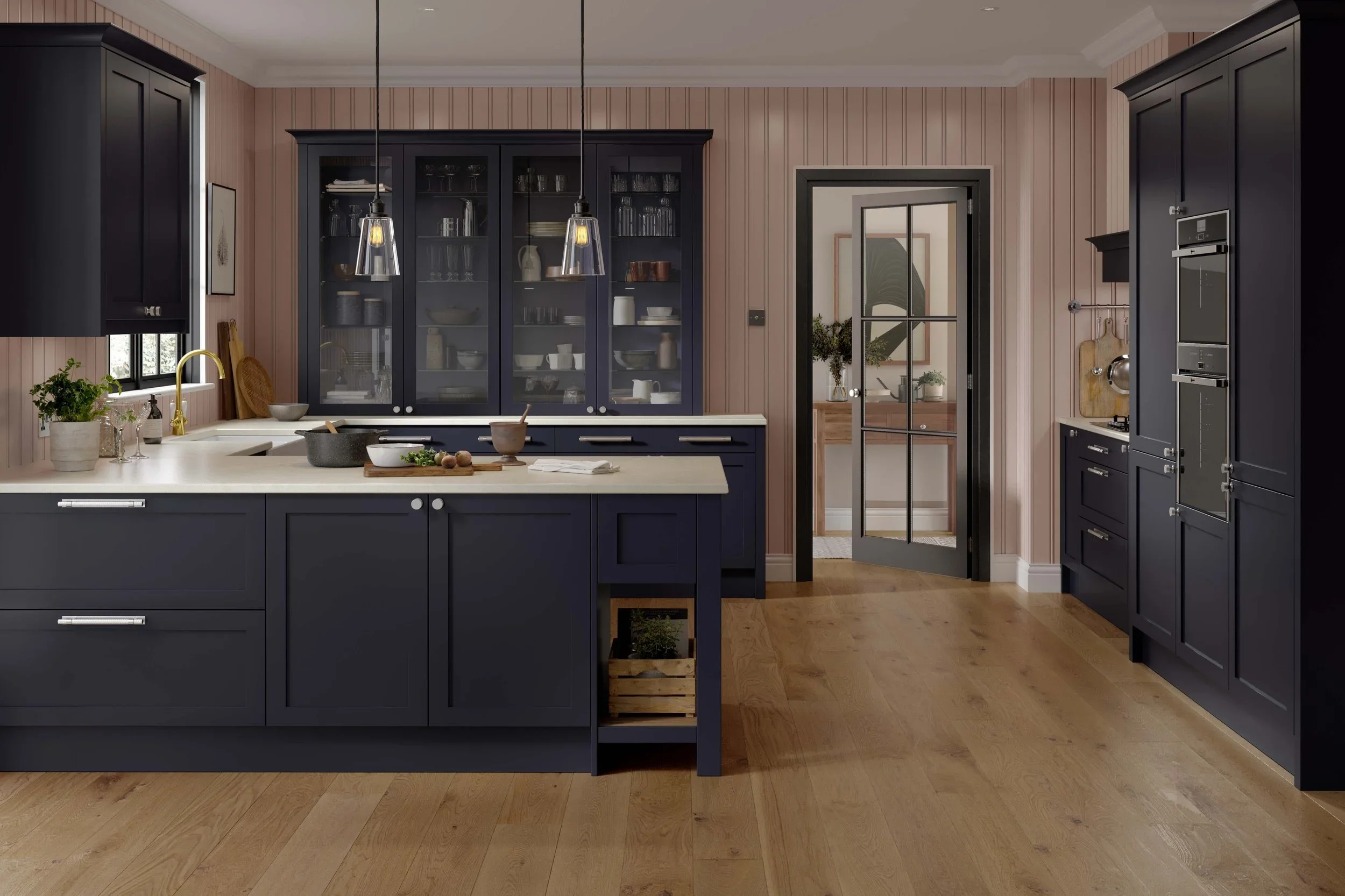 Modern kitchen with dark blue cabinets, light countertop, and wooden flooring. Features include a kitchen island with cooking utensils, pendant lighting, and a glass door leading to another room. The walls are panelled and have a subtle pink hue.