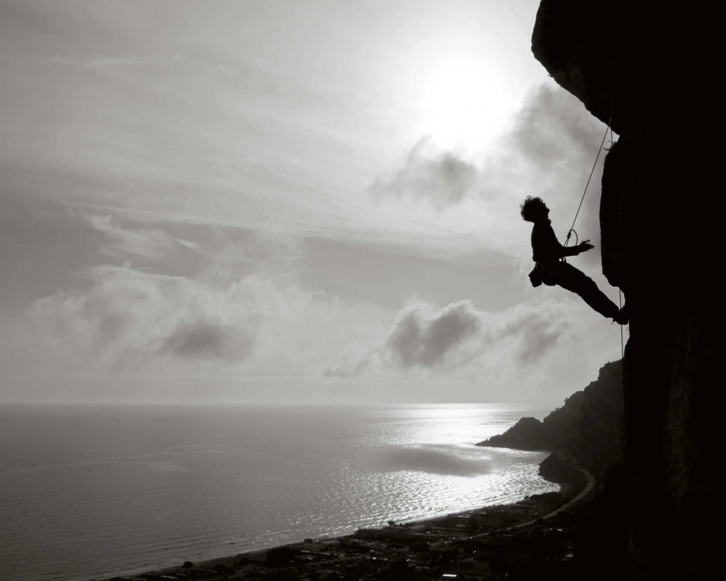 A man rock climbing on steep mountain side with harness