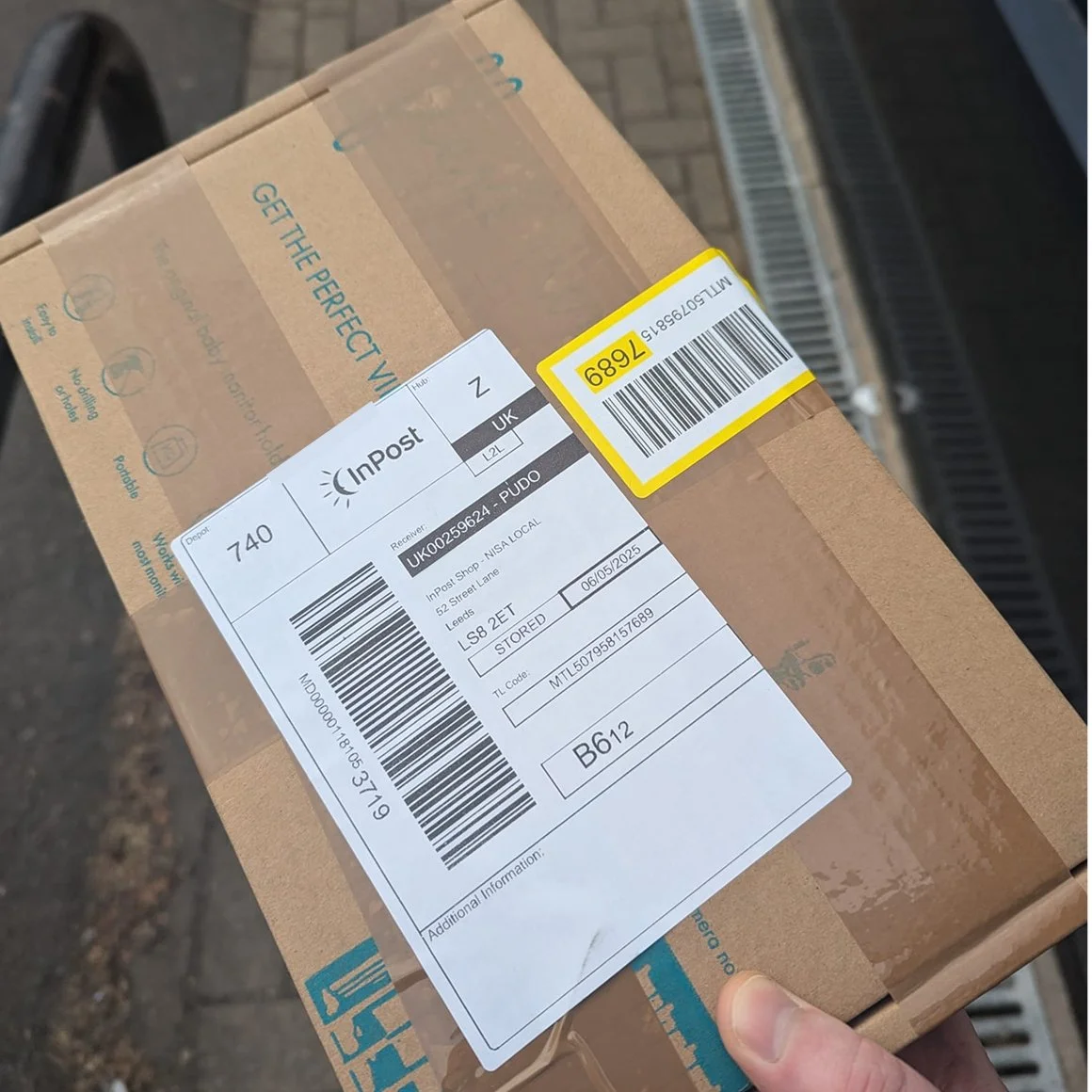 A cardboard package with a shipping label on it, being held outdoors on a brick sidewalk.