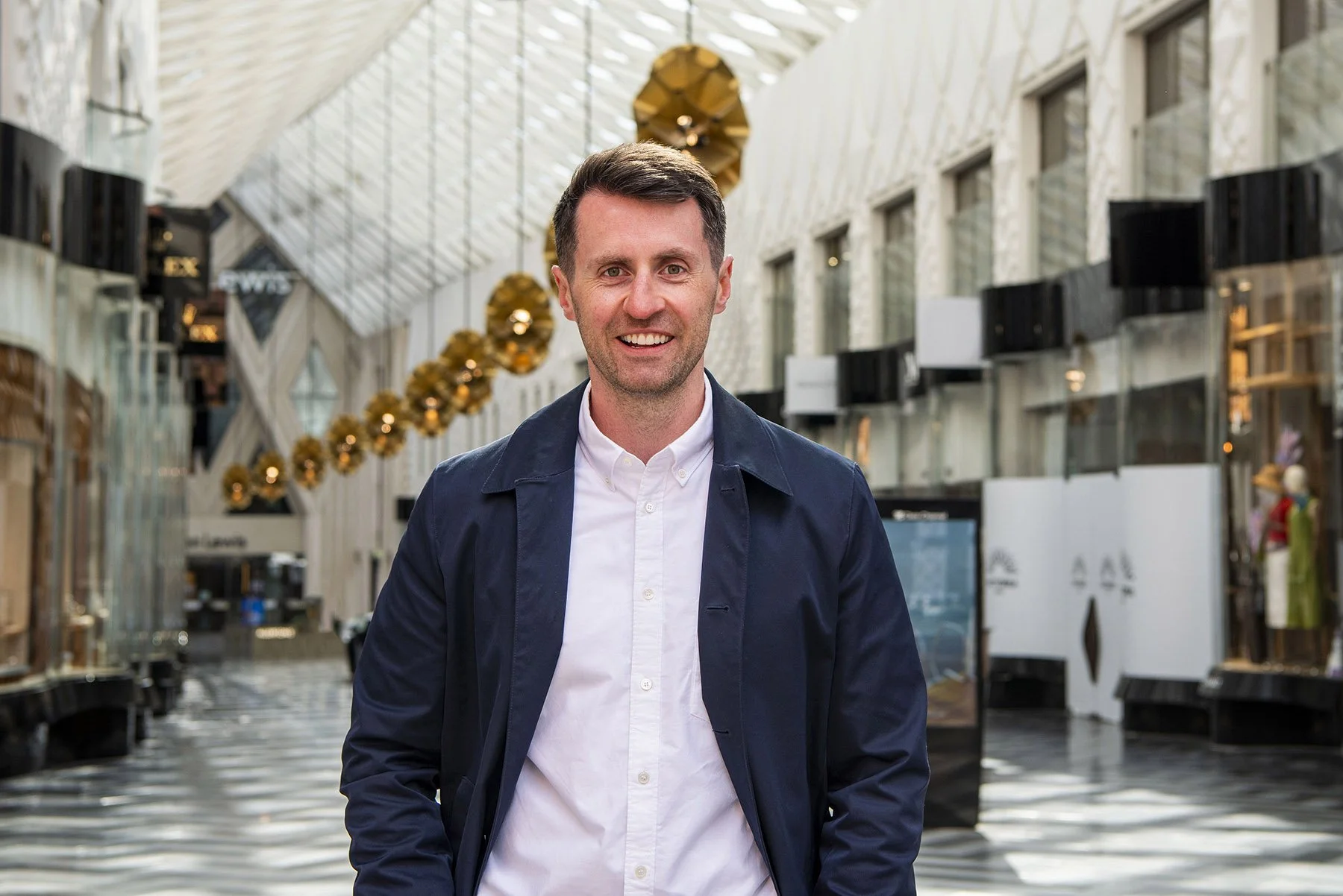 AAWE Founder and Managing Director, Tom Belt. Tom is wearing a white shirt and blue coat. Photo is taken at the entrance to Victoria Gate, Leeds.