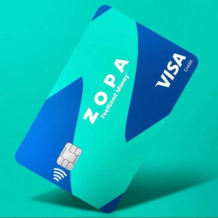 A ZOPA Visa credit card with a blue and teal design, positioned diagonally, showing the contactless payment symbol and the ZOPA logo with the tagline 'Feeling Good, Money'.