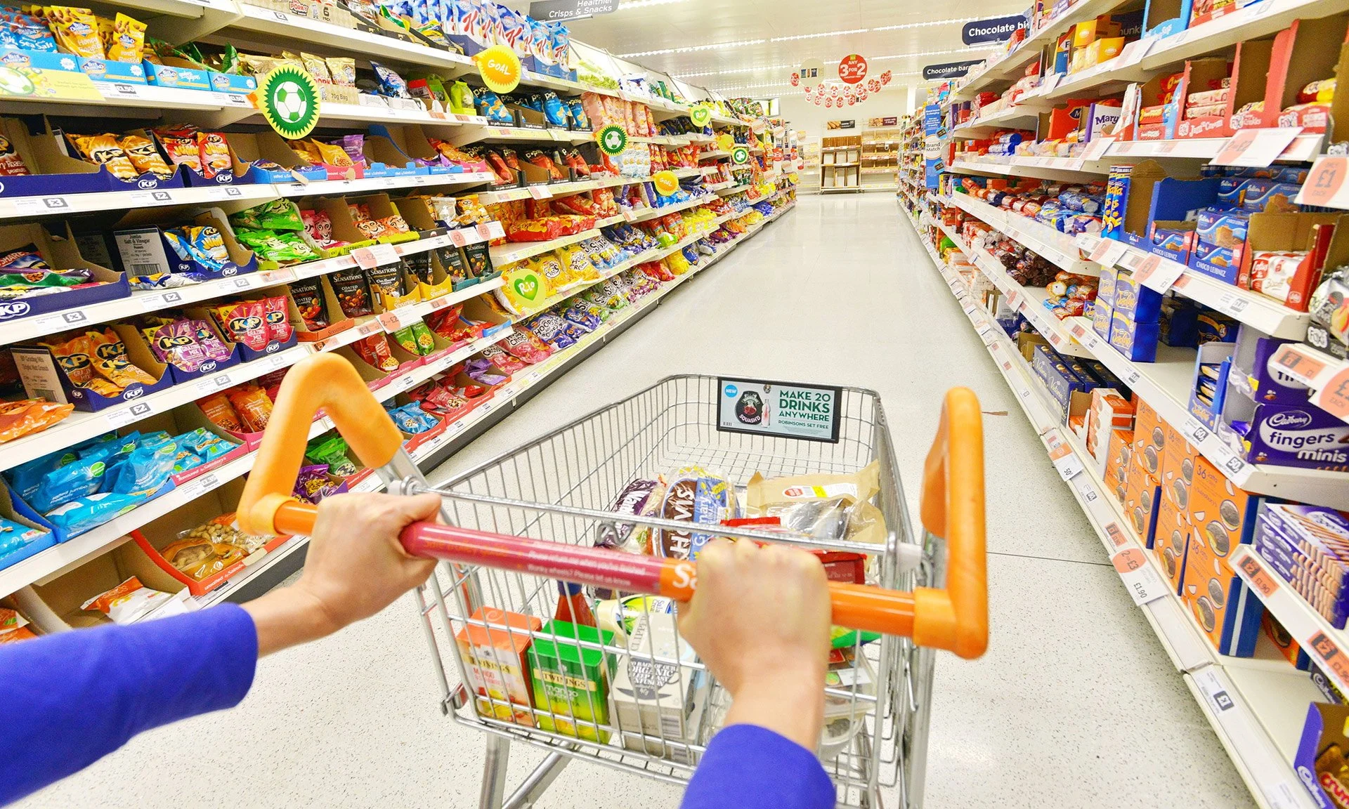 Customer pushing a trolley containing multiple items to purchase inside a grocery supermarket
