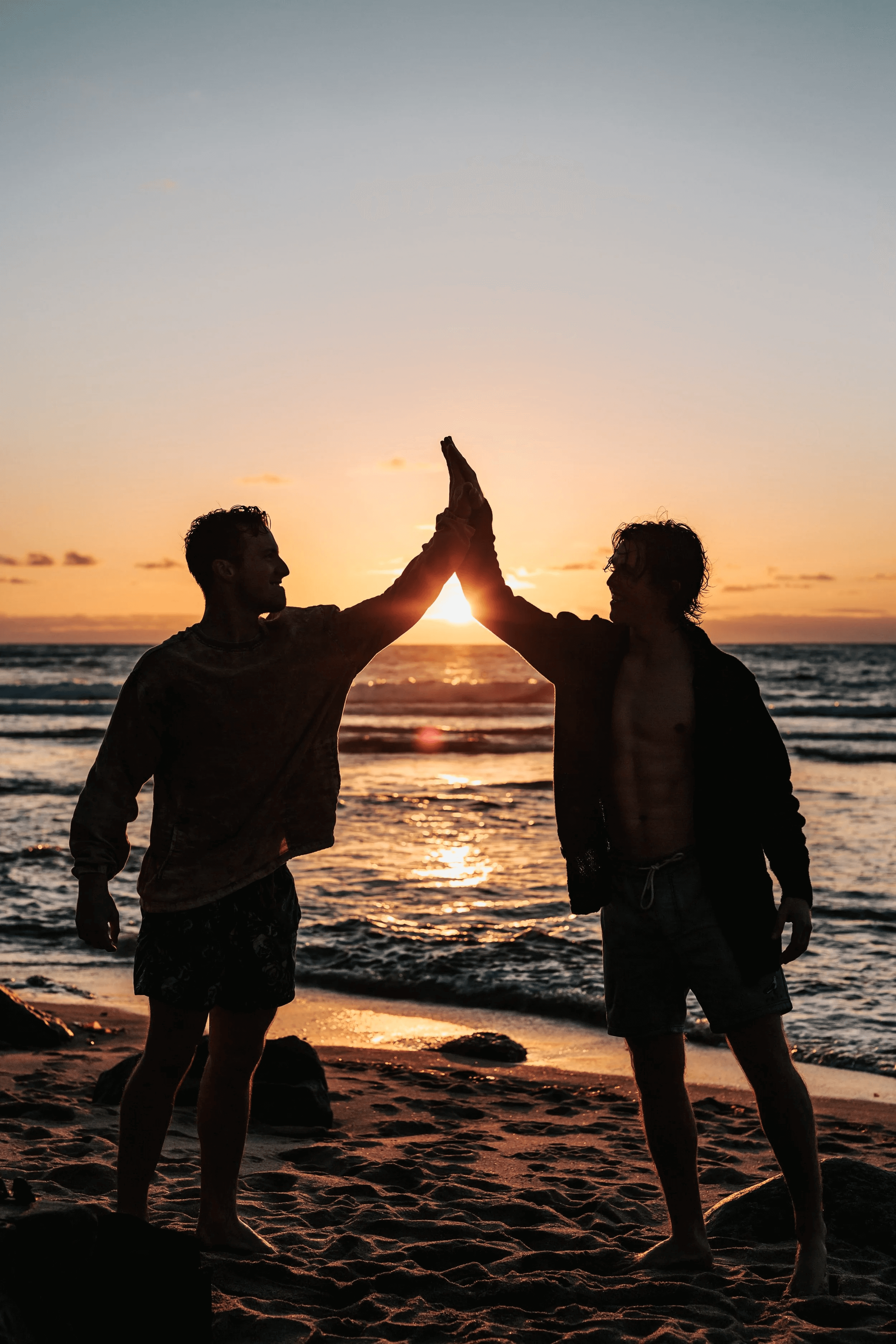 Two people high-fiving on a beach at sunset, representing a successful accident compensation claim outcome