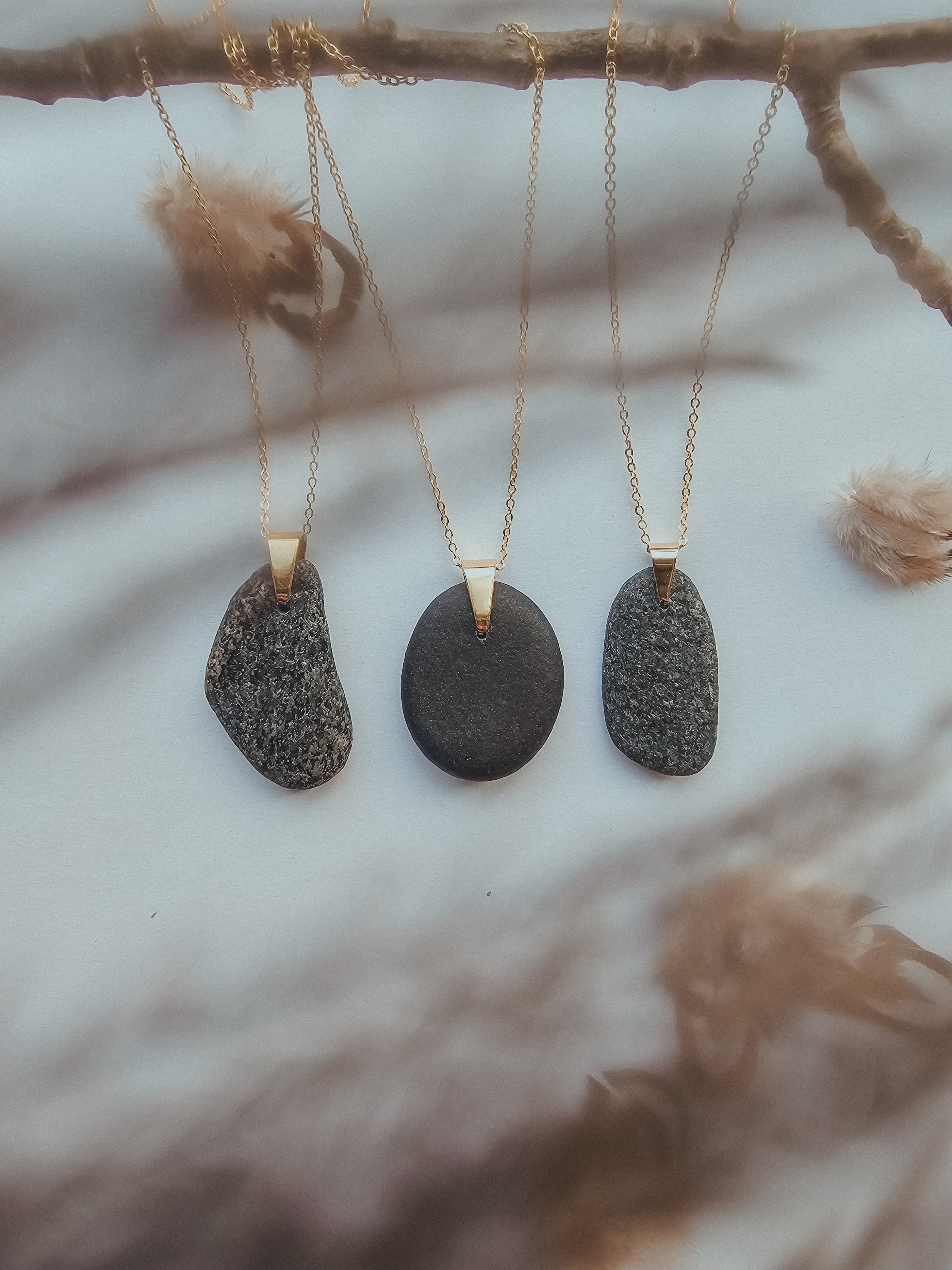 A trio of handmade Baltic Sea stone necklaces in various shapes and sizes, each featuring raw, sparkling pebbles on gold-plated chains.jpeg