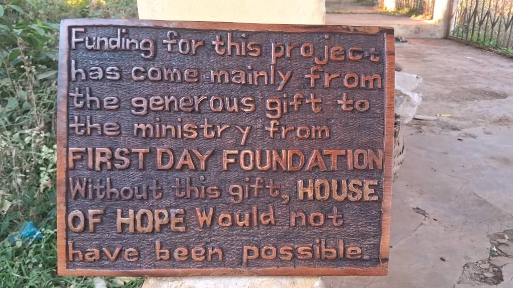 A metal plaque with an embossed message about funding from the FIRST DAY FOUNDATION, thanking generous gifts from the ministry and emphasizing the importance of hope for building a house.