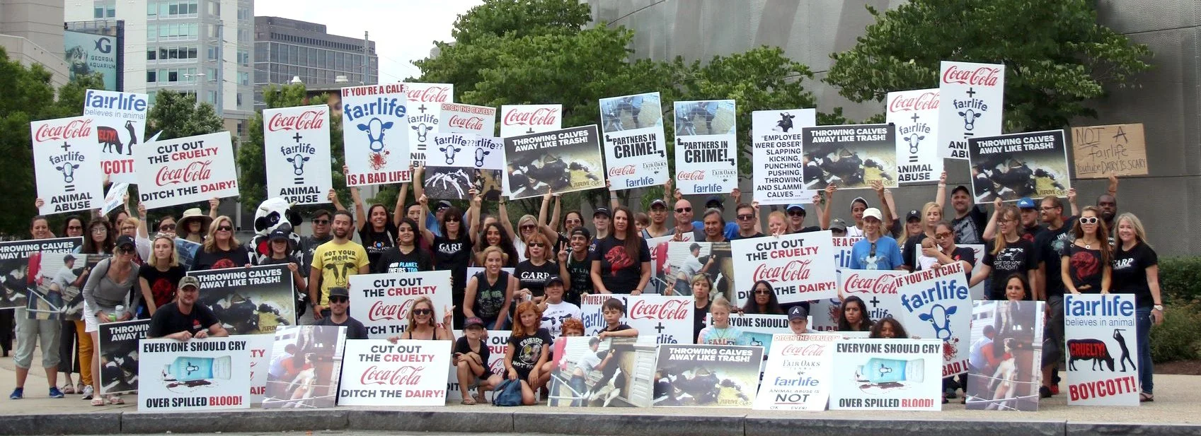 A large group of people protesting against animal cruelty, holding signs that say 'Cut Out the Cruelty', 'Ditch the Dairy', 'Everyone Should Cry Over Spilled Blood', and other messages about animal abuse and dairy industry cruelty.