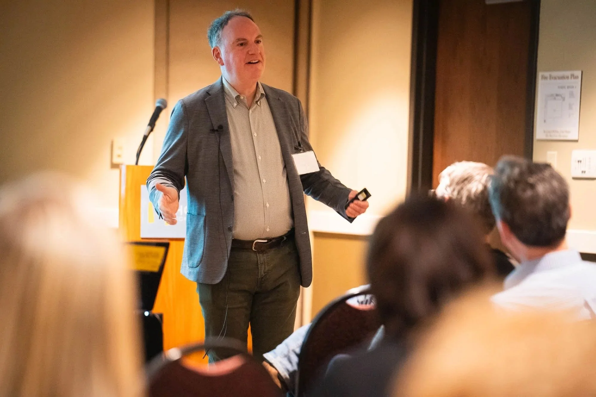 Photograph of  a man with his arms oustretched, presenting at a conference.