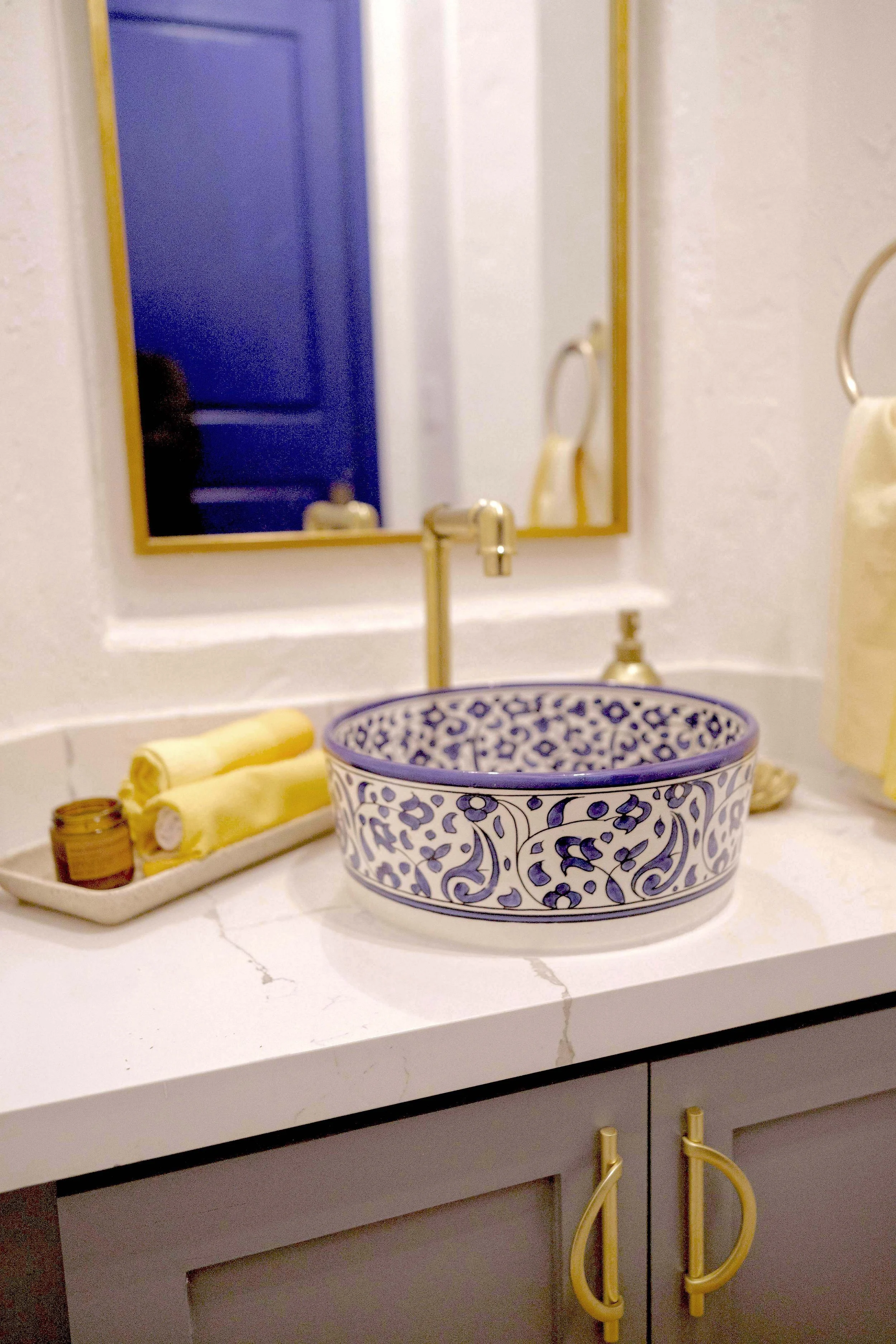 A round ceramic vessel sink with a floral cobalt and ivory pattern from Morocco is set atop a porcelain countertop to transport you even further into the vision.