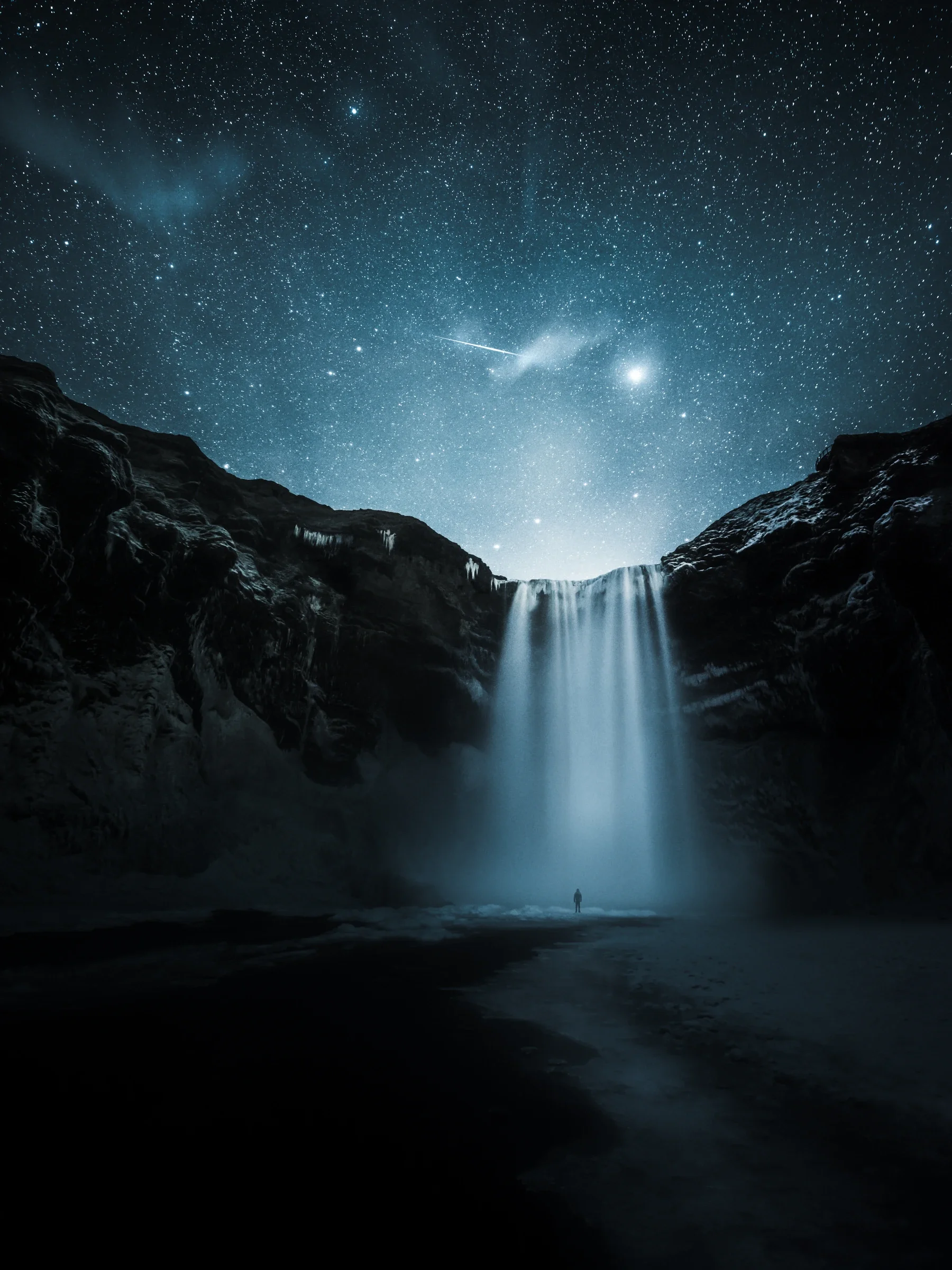 A tiny human silhouette standing in front of a massive waterfall.