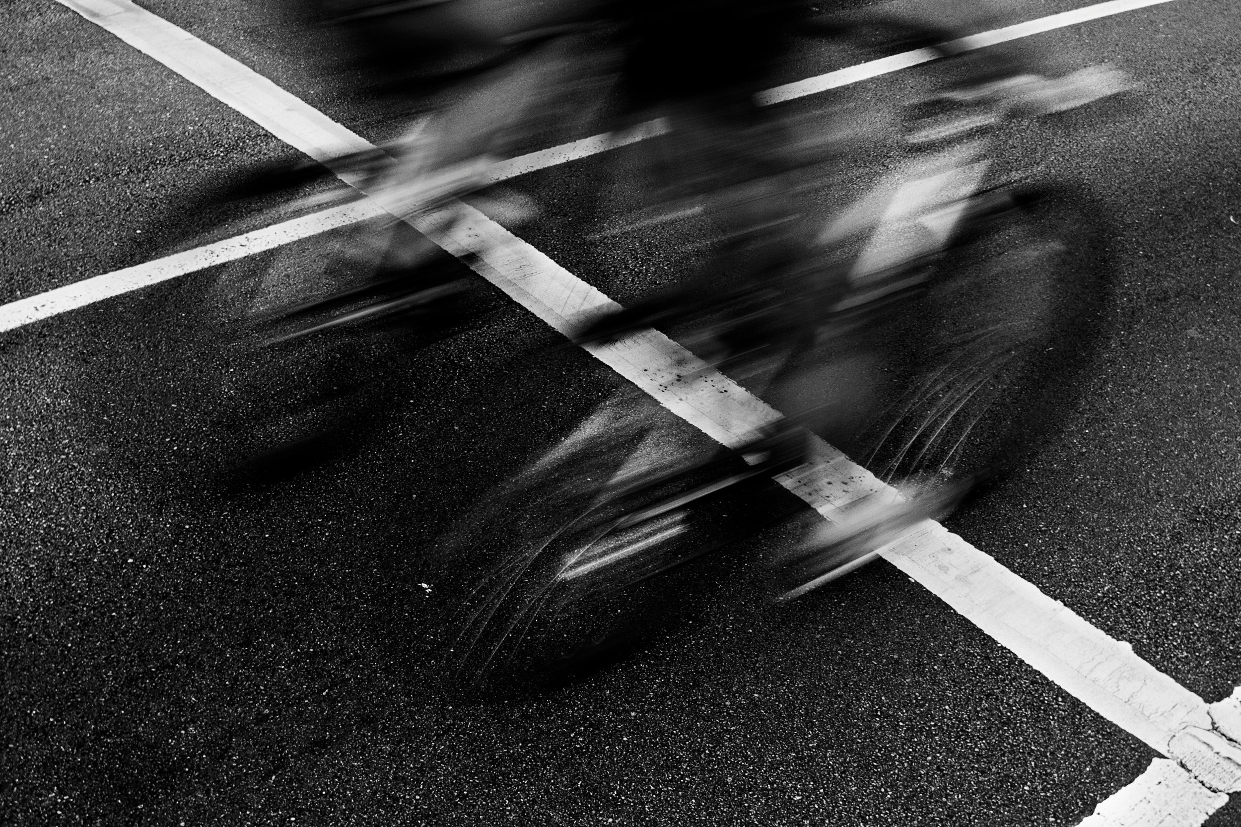 Blurred motion of two bicycles on a wet asphalt street with white painted lines.