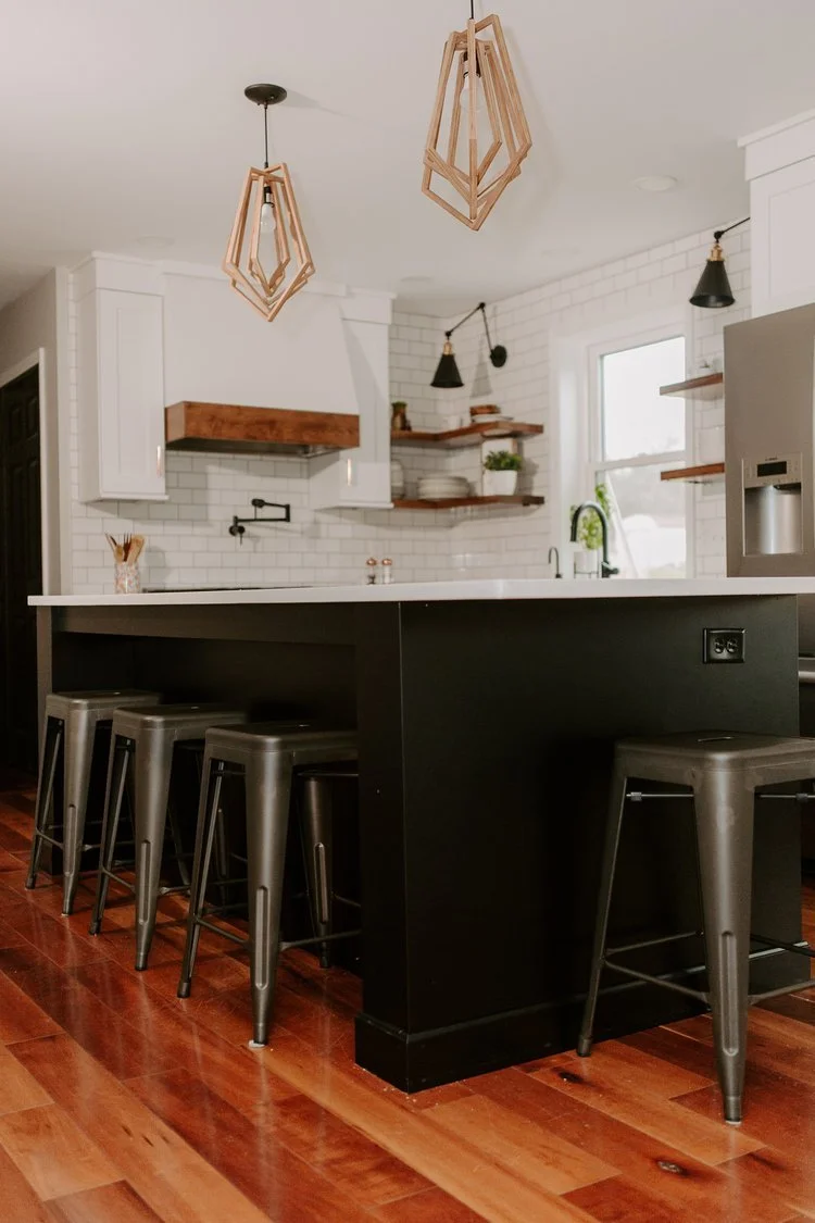 Engineered hardwood flooring extending through a modern kitchen with a black island, white cabinetry, subway tile backsplash, and wood pendant lights.