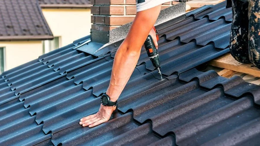 Close-up of roof construction with a worker fastening corrugated metal panels during installation on a residential home.