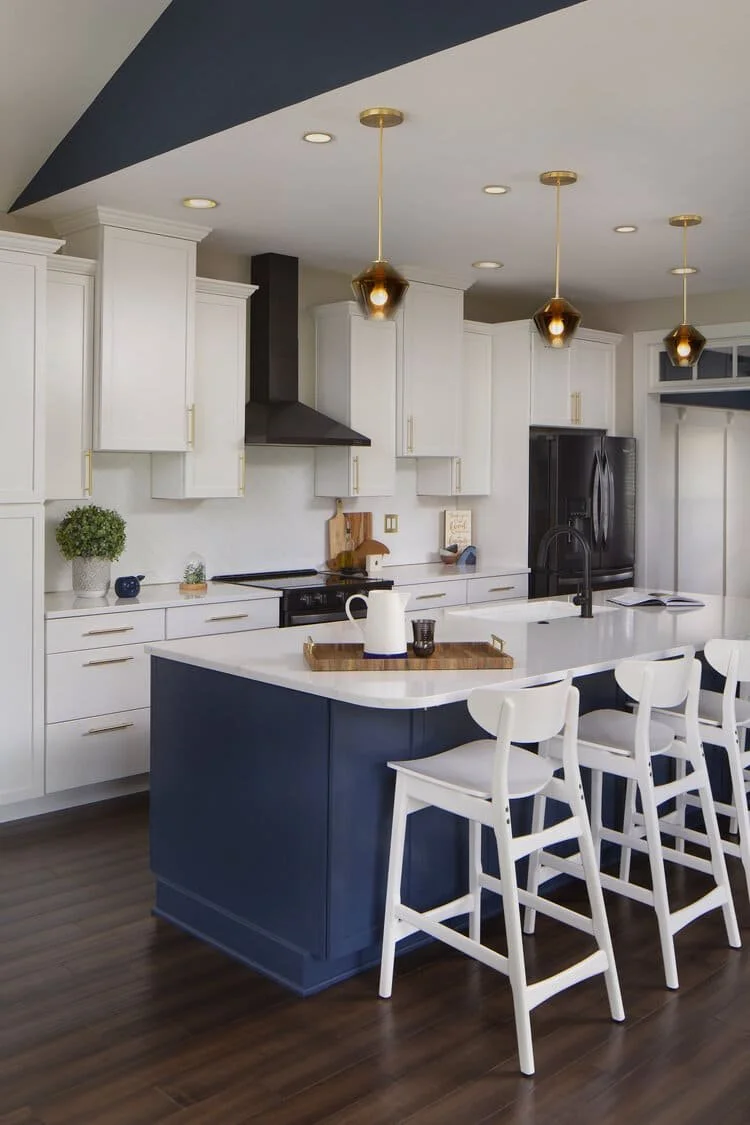 A modern kitchen features a navy blue island with white quartz countertops, white cabinetry, and white bar stools.