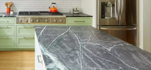 Kitchen island with a dark soapstone countertop featuring distinct white veining, set against sage green cabinets