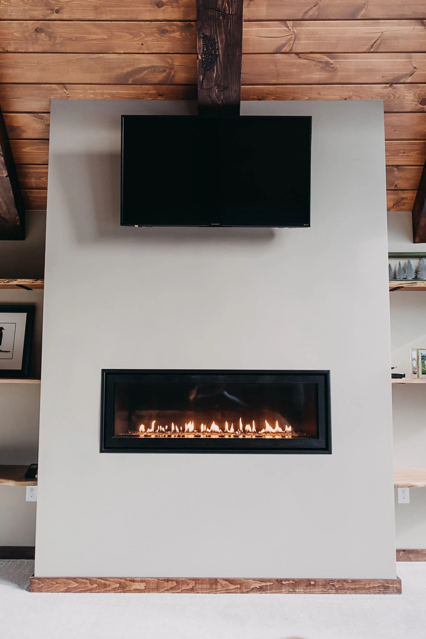 Custom fireplace and media wall featuring a linear fireplace, mounted TV, built-in shelving, and exposed wood ceiling beams.