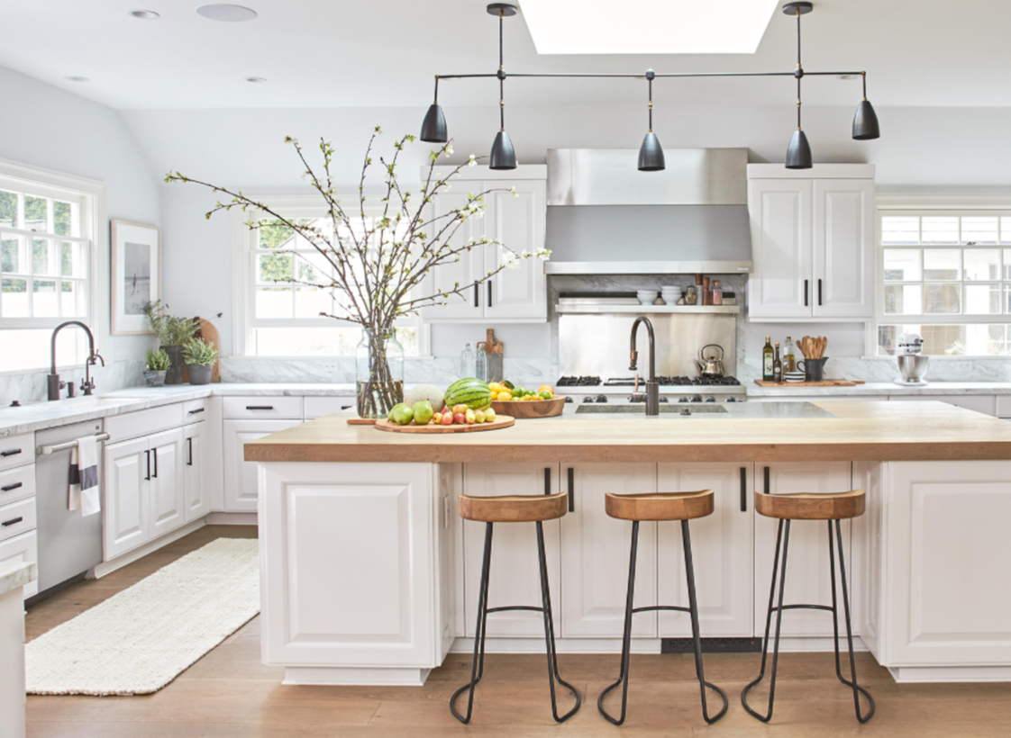 Bright modern kitchen with a large butcher block island, matching wooden barstools, white cabinetry, and marble countertops.