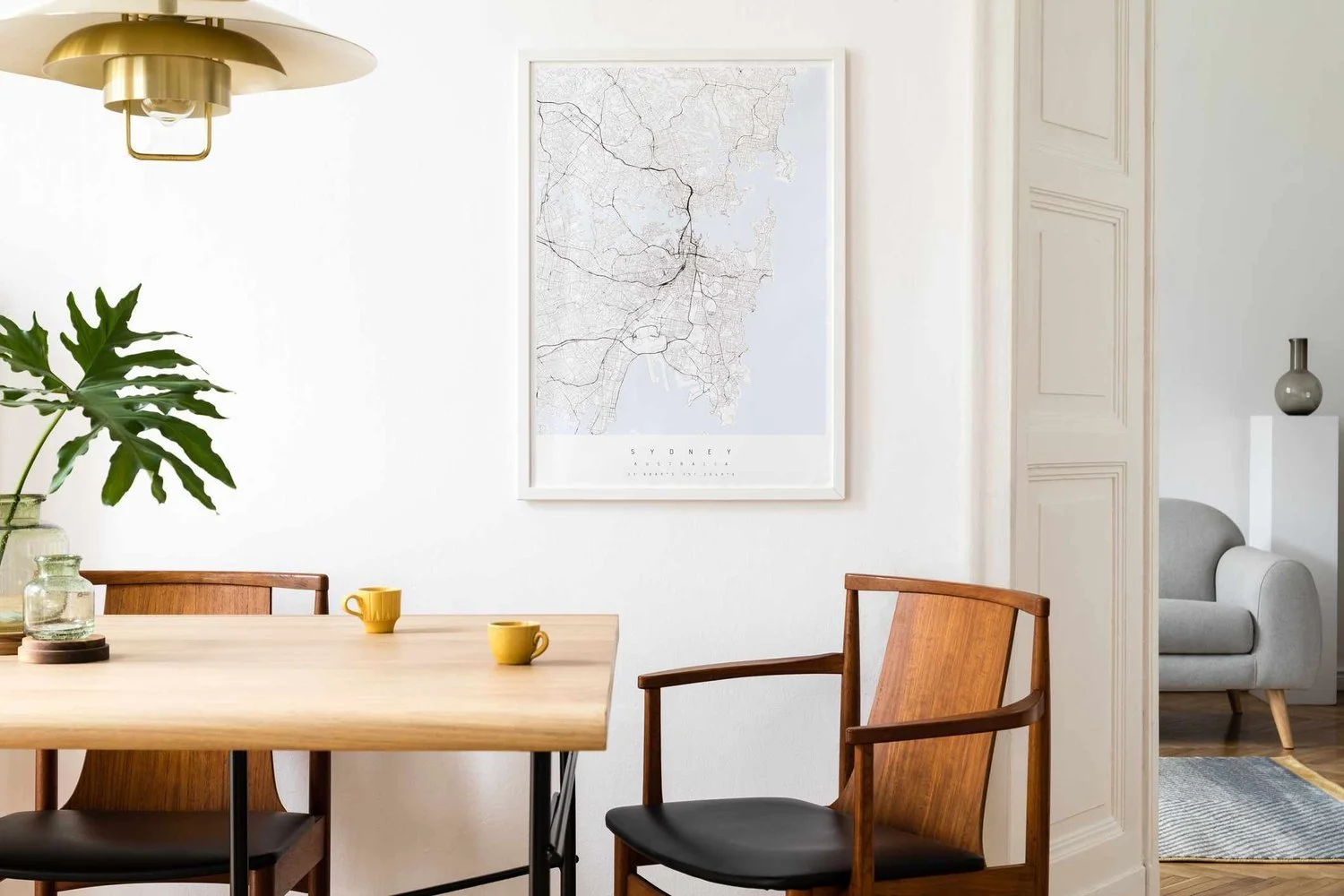 Minimalist dining room with a wooden table, mid-century modern chairs, city map artwork, brass pendant light, and green plant.