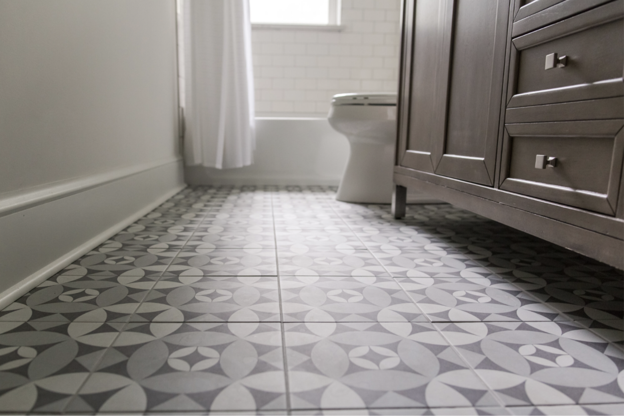 Stylish bathroom with gray patterned floor tiles, a gray vanity, silver hardware, and a white bathtub with a curtain.