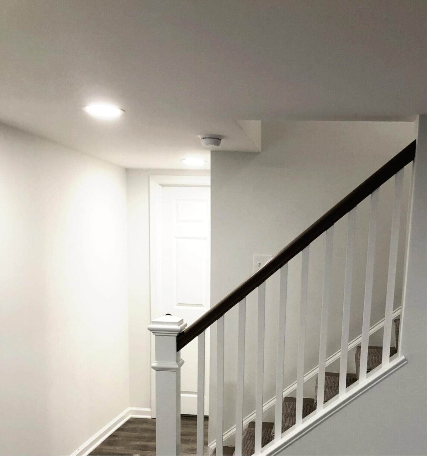 Modern home hallway featuring custom-style white balusters, a decorative newel post, dark wood handrail, and recessed lighting.