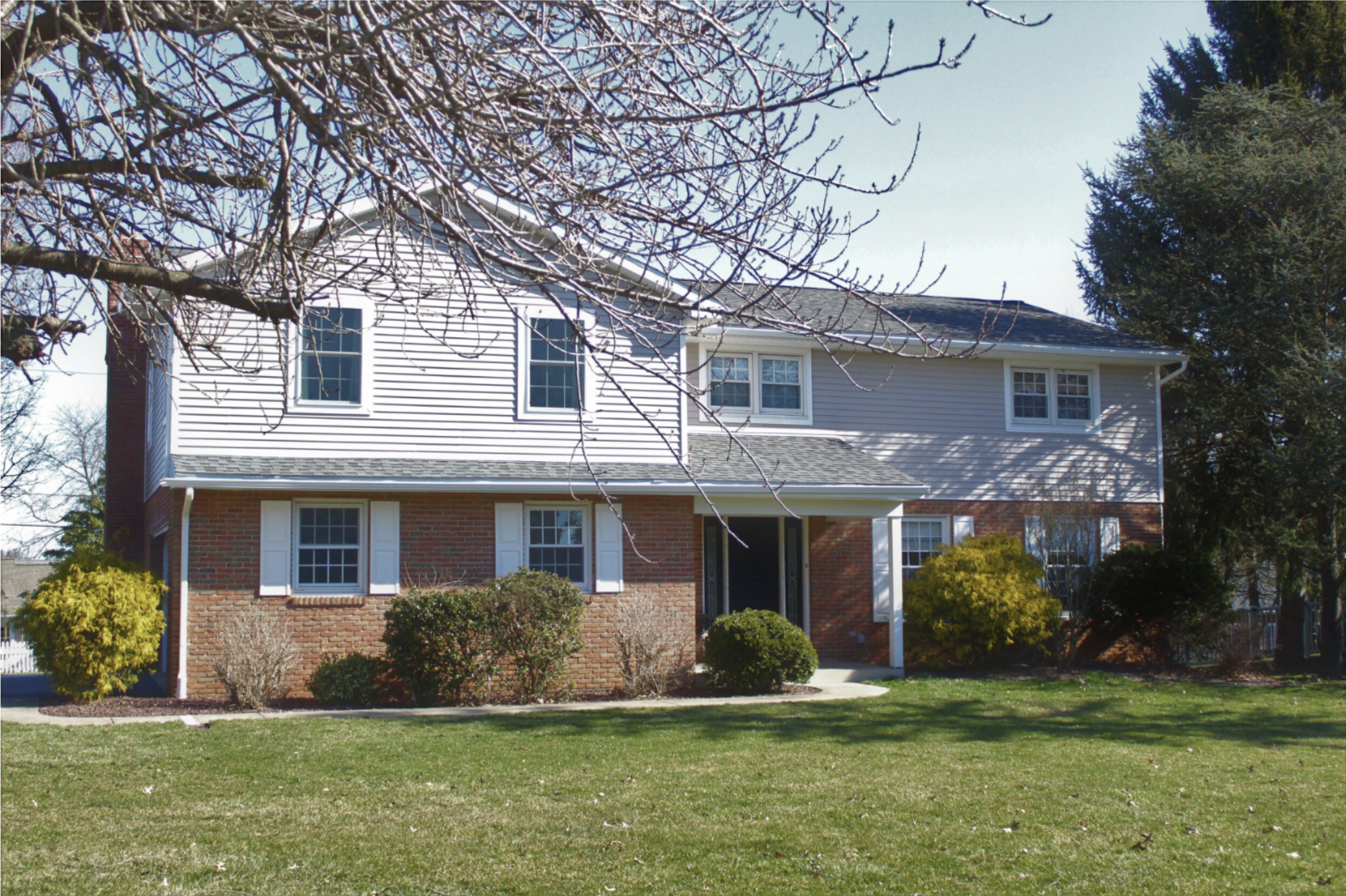 Exterior view of a two-story brick and siding house with landscaped bushes and a front walkway