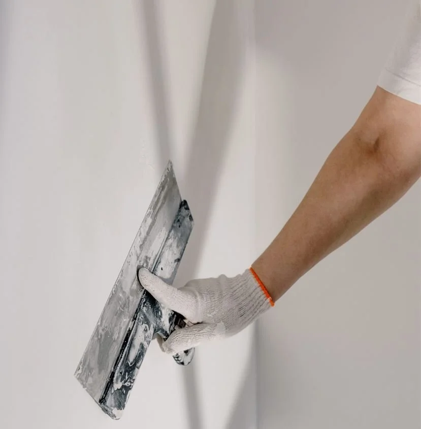 Close-up of a worker using a drywall taping knife to apply and smooth joint compound during interior remodeling.