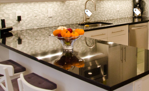 Contemporary kitchen featuring a luxurious dark granite island, white cabinetry, mosaic tile backsplash, stainless steel faucet, and decorative fruit bowl.