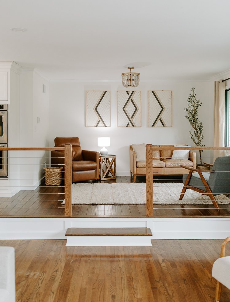 Hardwood flooring in an elevated living room with a custom wood railing, leather seating, textured rug, and geometric wall art.