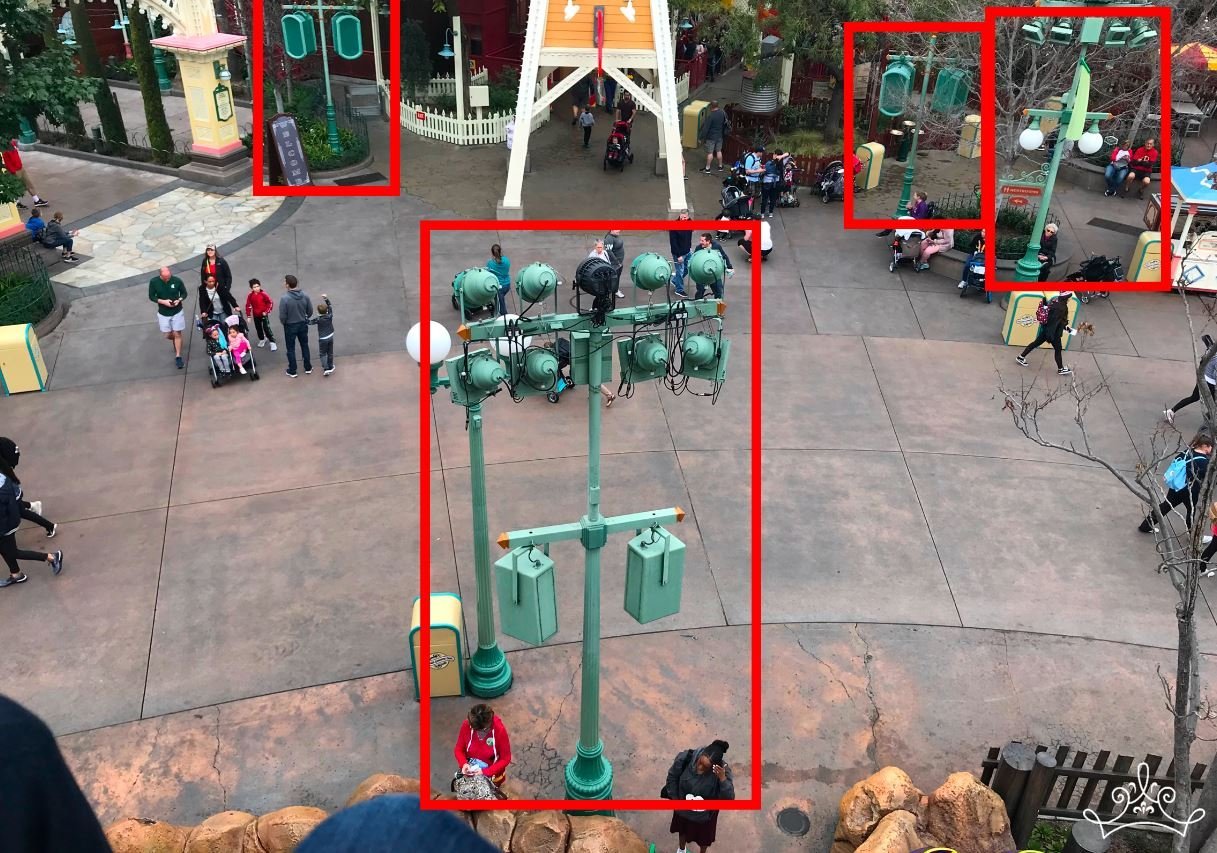 An elevated view of a theme park plaza with lampposts and utility fixtures outlined in red to illustrate Disney’s go-away green paint technique.