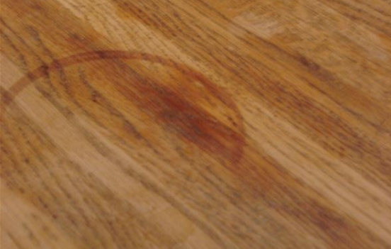 Angled close-up of a wooden countertop showing a prominent circular moisture stain against its textured wood grain.