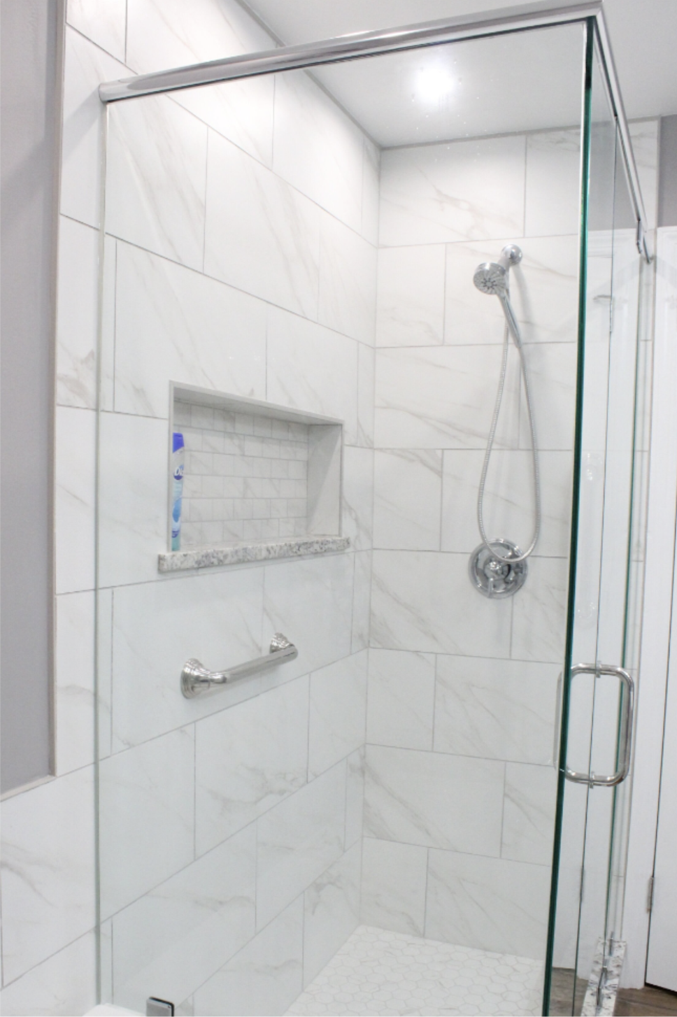 Modern walk-in glass shower interior featuring white marble-look tiles, a built-in niche, and chrome fixtures