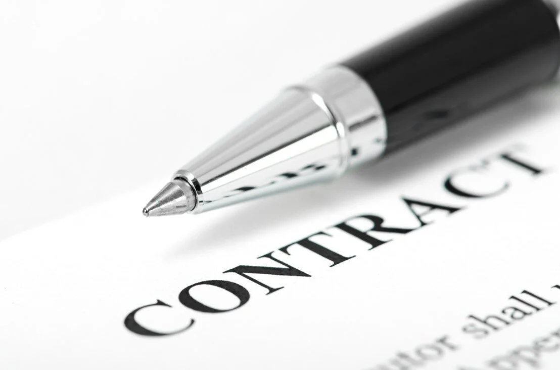 Metallic pen positioned over a document labeled “CONTRACT,” illustrating the process of reviewing and signing a home remodeling agreement.