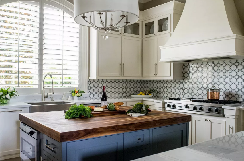 Luxurious kitchen featuring a deep blue island with a thick wood butcher block countertop, white cabinetry, and patterned tile backsplash.