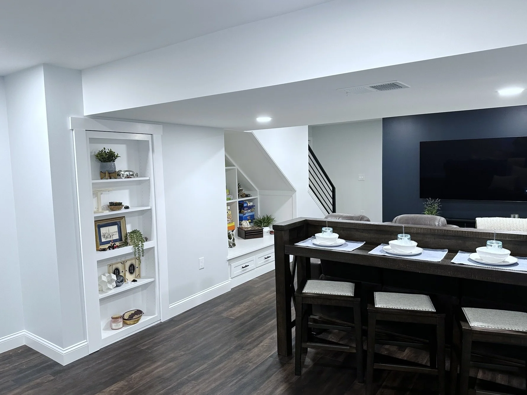 Finished basement remodeling project with a dark wood bar table, custom shelving, under-stair storage, and a mounted TV.