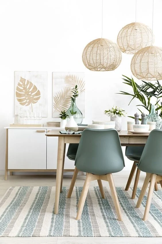 Minimalist dining room featuring sage green chairs, a light wooden table, striped rug, white sideboard, and natural accents.