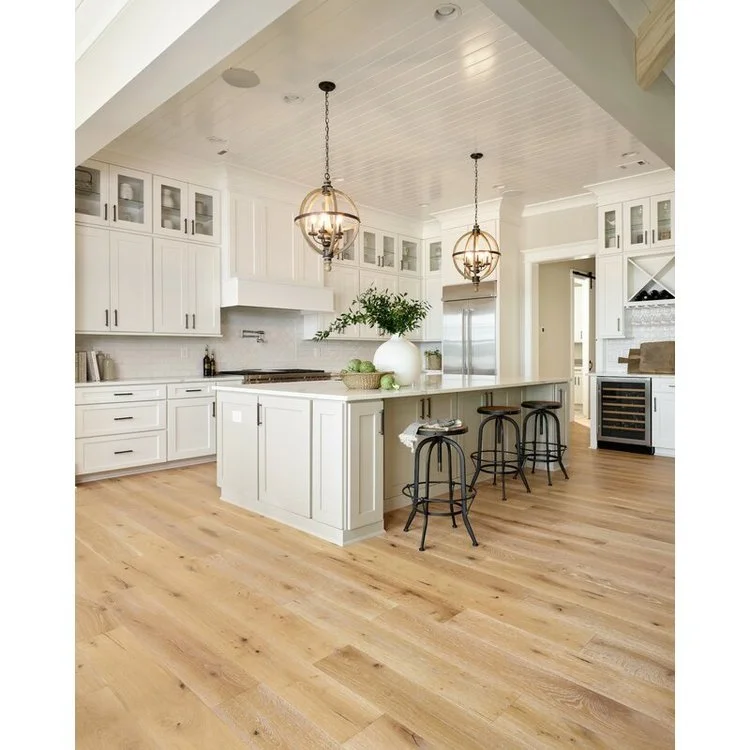 Spacious kitchen with light wood flooring, white cabinetry, stainless steel appliances, and a large island beneath distinctive orb pendant lights.