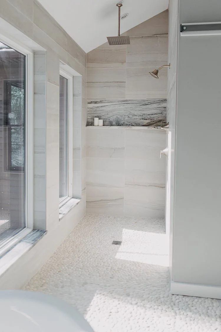 Natural stone shower flooring featuring textured white pebble tiles, marble-look walls, and a recessed shower niche.