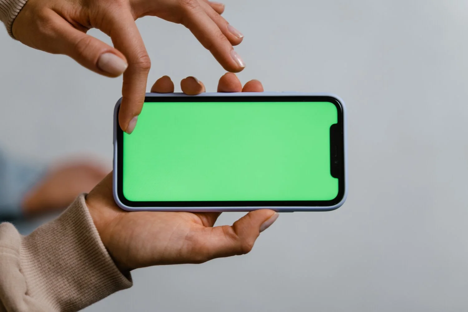 A person holding a smartphone horizontally with both hands and interacting with the green screen.