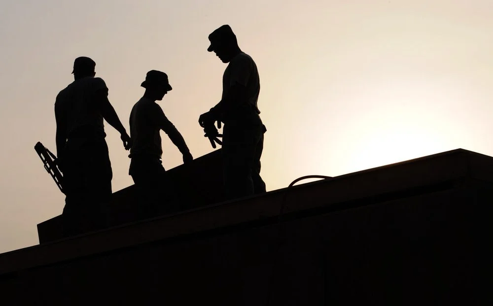 Three construction workers standing on a building roof against a bright sunset sky during a project.