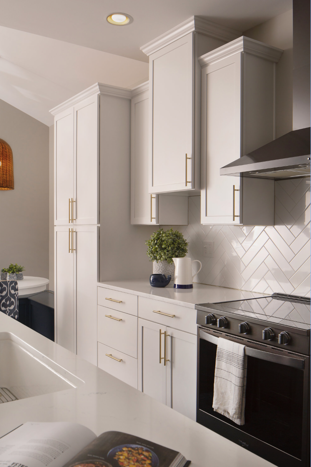 Custom kitchen cabinetry includes tall pantry cabinets, white shaker doors, gold hardware, quartz countertops, and a decorative plant.