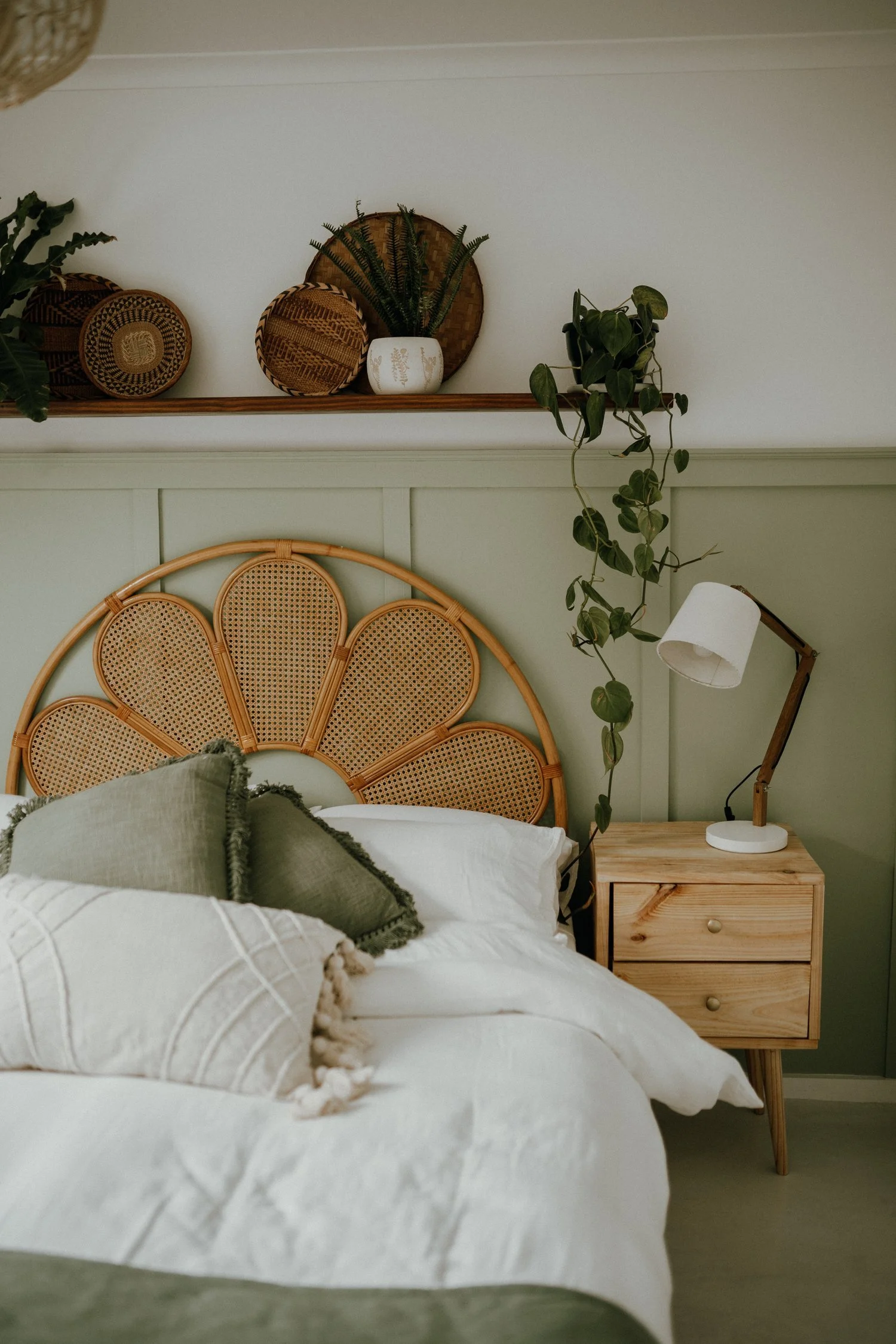 Serene Scandinavian bedroom with a sage green paneled wall, scalloped rattan headboard, white bedding, and light wood accents.