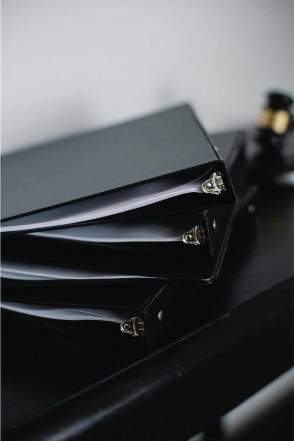 Stack of black three-ring binders containing white documents, neatly arranged on a dark desk for organized document storage.