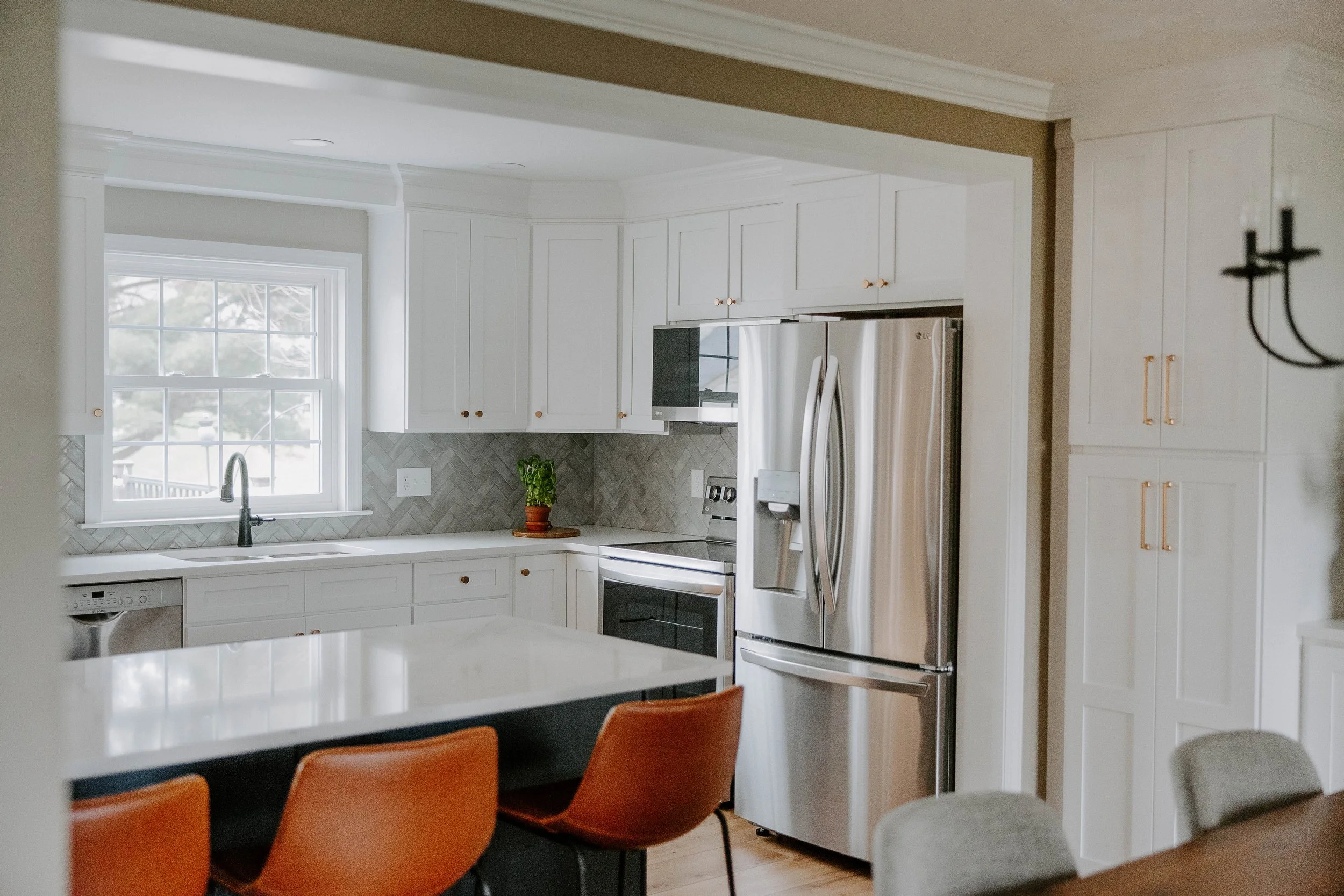 Bright white kitchen with quartz countertops, a central island, stainless steel appliances, and herringbone backsplash completed by Vatter Construction.